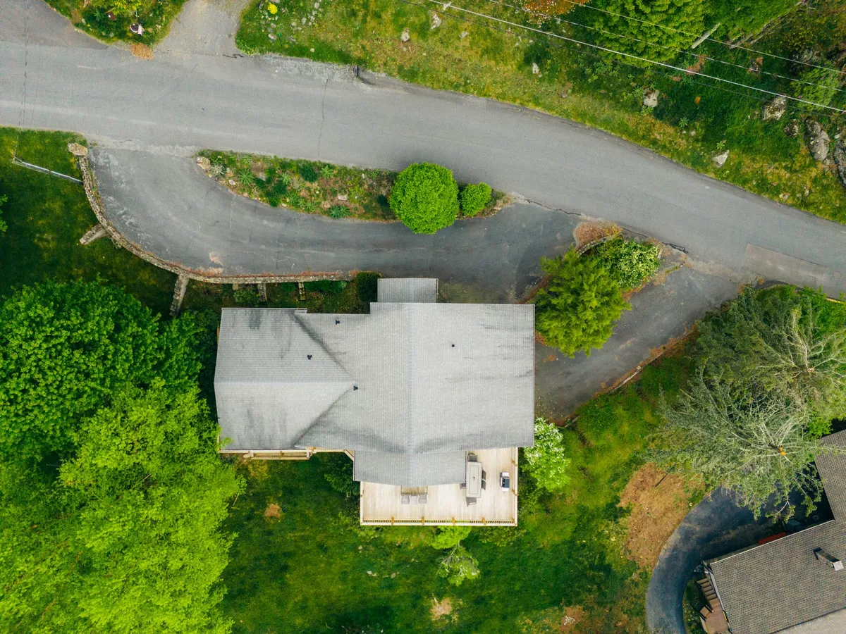 This exterior image showcases Hawk Haven nestled amid lush greenery, with a winding road leading up to the house. The setting radiates peace and seclusion, with a sizable deck ideal for relaxing and watching sunsets, and a yard surrounded by mature trees.