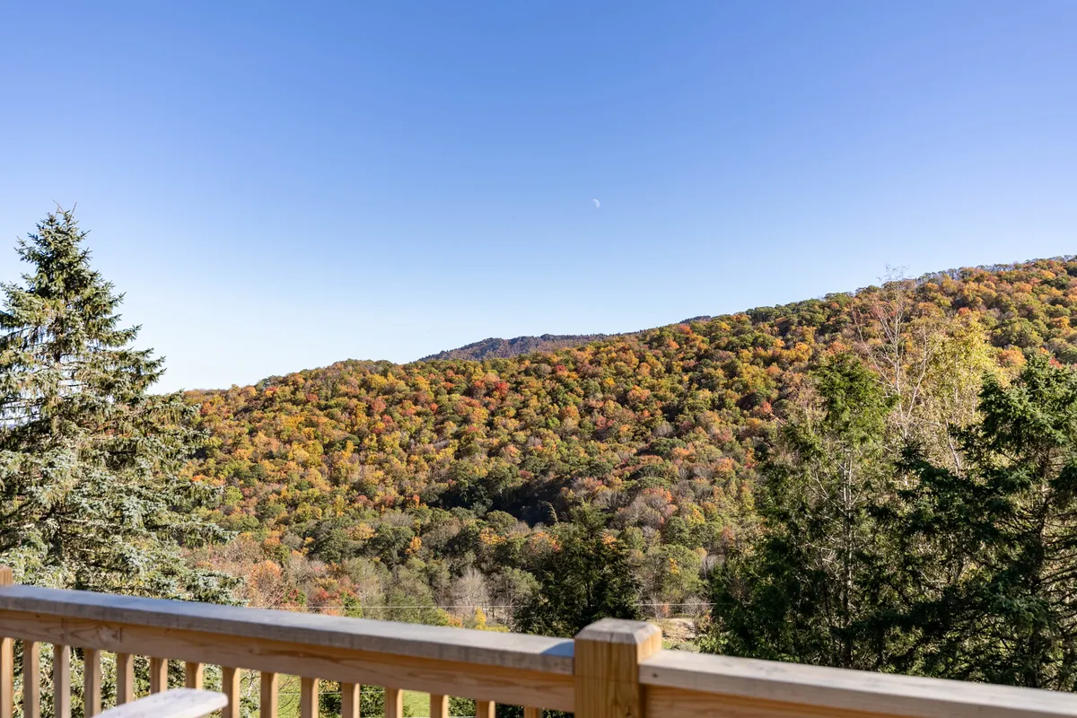 A breathtaking panoramic view of the Blue Ridge Mountains featuring rolling hills blanketed in vibrant autumn foliage, a clear blue sky, and distant mountain peaks. The tranquil scene invites outdoor activities like hiking, bird watching, and photography, with hints of early morning fog and the promise of colorful sunsets.