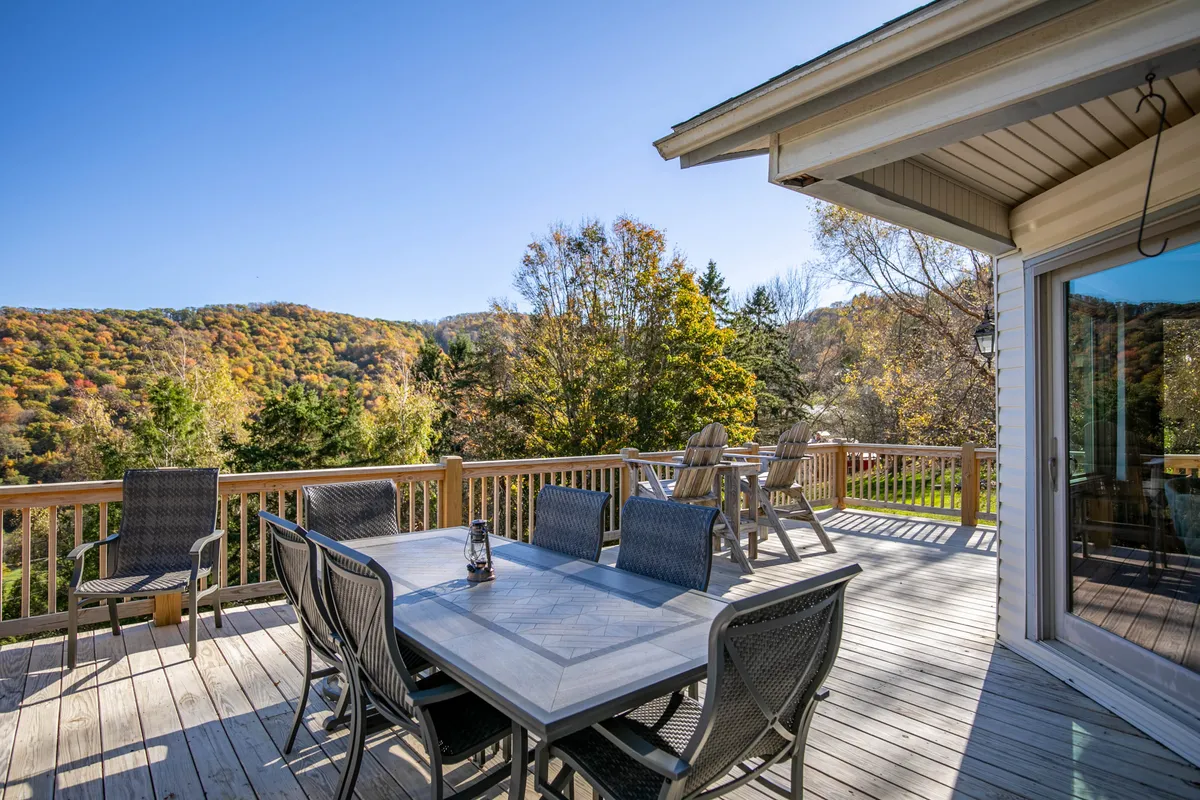 This image features an outdoor dining table on a deck with a wooden railing, facing stunning mountain views and vibrant fall foliage. The setting is inviting for relaxation after a day of activities, with space for family gatherings and celebrations.