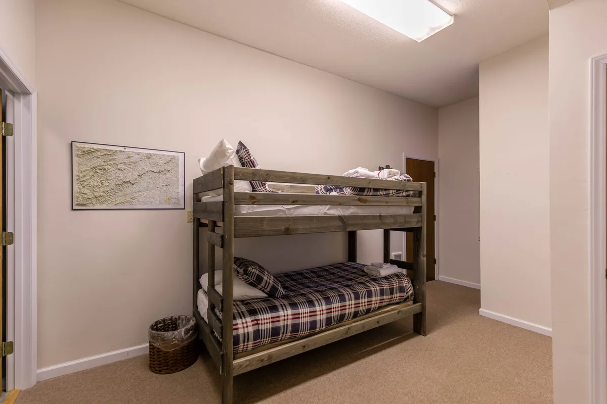 A cozy alcove outfitted with a twin over twin bunk bed dressed in playful plaid bedding, accentuated by a framed map on the wall. The compact design creates a fun, inviting nook perfect for kids or adventurous guests.