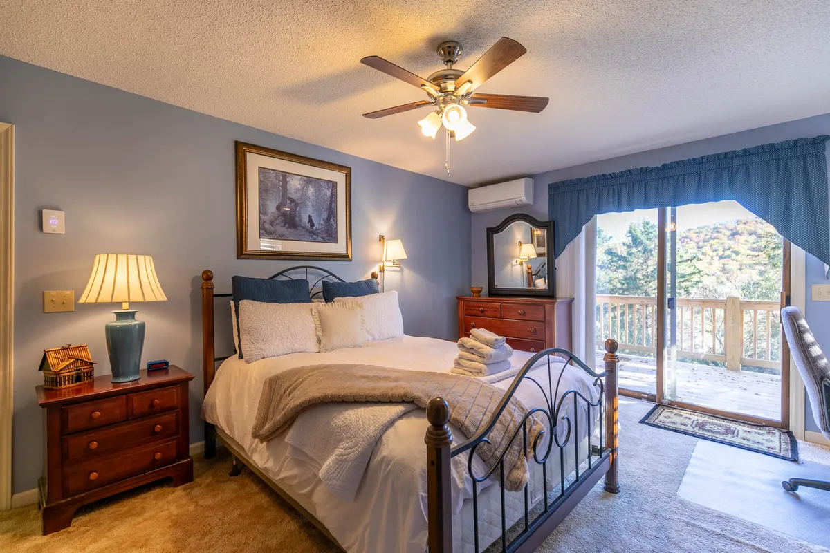 A tranquil bedroom with plush bedding, a large window overlooking the outdoors, a wooden dresser, and a decorative lamp. The scene is serene and inviting, emphasizing privacy and comfort for restful nights and quiet moments.
