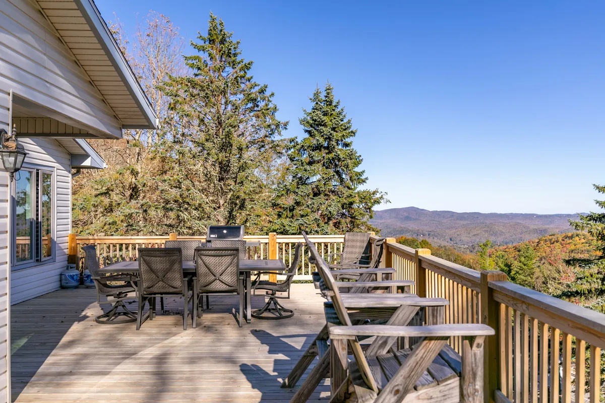 A serene deck scene with a dining table and several chairs arranged to enjoy a panoramic mountain view. The table is set for a gathering, inviting guests to relax, dine, and take in the sunset over the mountains.