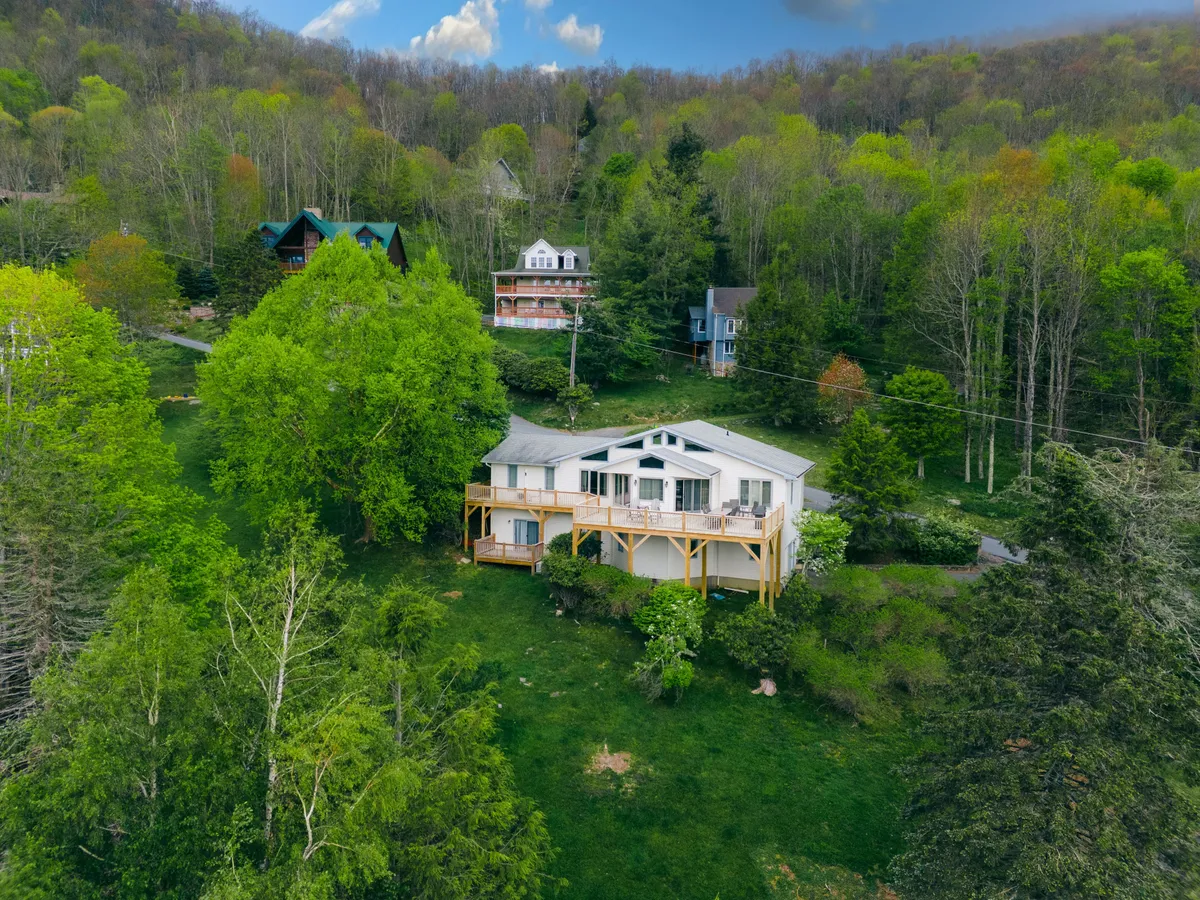 An exterior view of the main house set among verdant greenery, with neighboring houses nearby. The scene evokes a serene, natural environment that is perfect for enjoying nature walks, hosting family gatherings on the deck, or stargazing on clear nights.