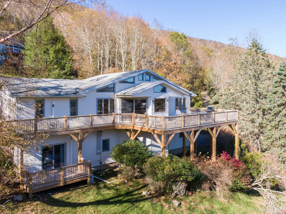 A spacious wooden deck with panoramic windows and a beautifully landscaped garden, offering ample space for outdoor gatherings. The deck features comfortable seating and is surrounded by lush greenery, making it ideal for relaxing, enjoying mountain views, or stargazing at night.