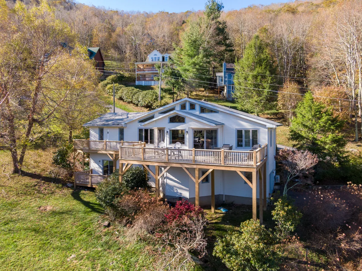 The image presents a spacious deck with railing, large windows, and surrounding trees. The landscaped yard and tranquil setting evoke a welcoming atmosphere, ideal for enjoying nature and planning the next day's adventures.