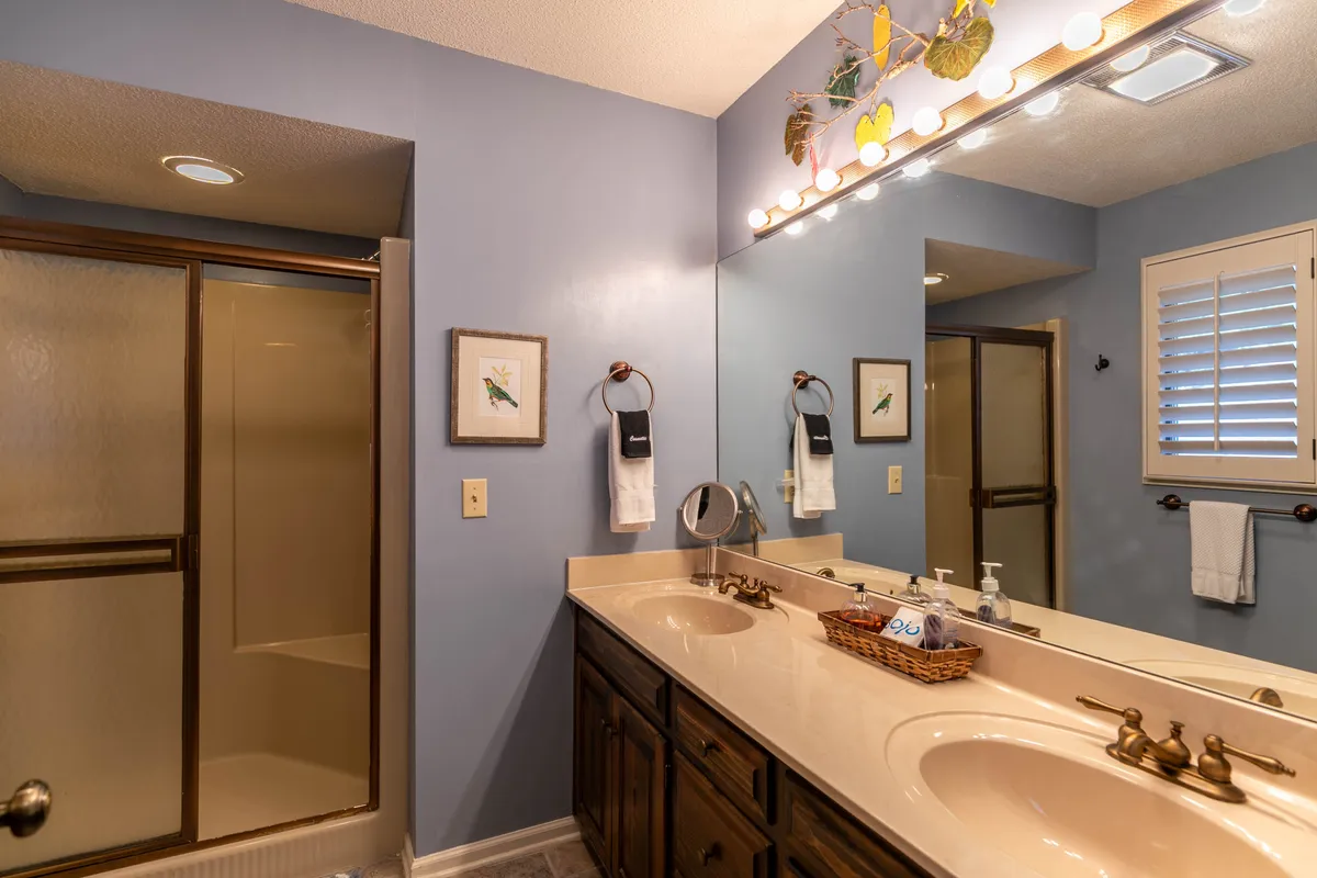 A modern bathroom with a double vanity, contemporary lighting, framed bird artwork, and a spacious shower area. The space is bright, fresh, and organized for daily routines or relaxation.
