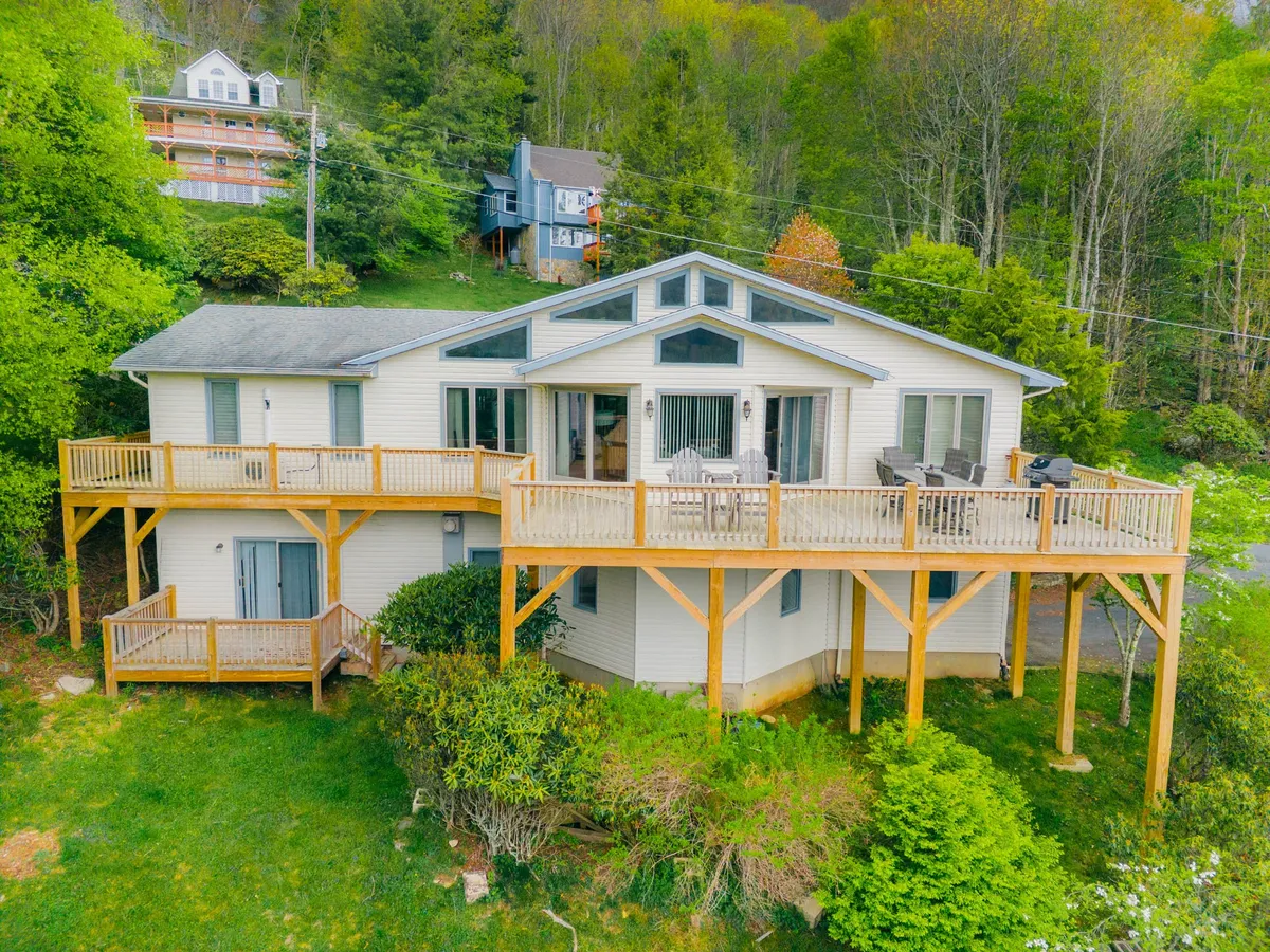 An inviting, spacious deck surrounded by greenery and featuring comfortable outdoor seating. The deck offers a seamless transition between the home and nature, with views of lush foliage and hints of mountain landscapes beyond. It's ideal for morning coffee, evening gatherings, and stargazing under open skies.